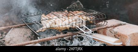 Hühnerfleischfutter werden auf dem Grill auf schwelenden Kohlen oder vom Lagerfeuer am Boden am Sommer- oder Herbsttag gebraten. Grill in Campingbedingungen. Sur Stockfoto