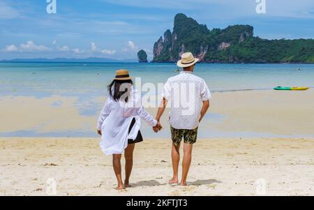 Ein paar Männer und Frauen, die in der Morgensonne am Strand spazieren. Loh Dalum Beach Koh Phi Phi Stockfoto