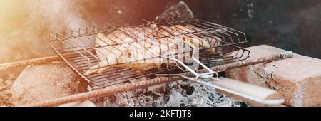 Huhn Fleisch Essen gebraten Grill auf schwelende Kohlen oder Ember vom Lagerfeuer auf dem Boden am Sommer oder Herbsttag. Grill in Camping-Bedingungen. Überleben o Stockfoto