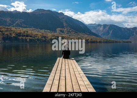 Sitzen auf einem kleinen Steg und genießen den Blick auf die Landschaft des Bohinjer Sees im Triglav Nationalpark, den Julischen Alpen, Slowenien Stockfoto