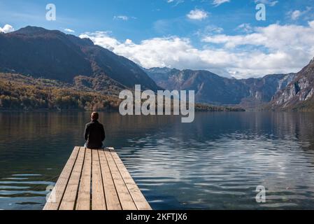 Sitzen auf einem kleinen Steg und genießen den Blick auf die Landschaft des Bohinjer Sees im Triglav Nationalpark, den Julischen Alpen, Slowenien Stockfoto