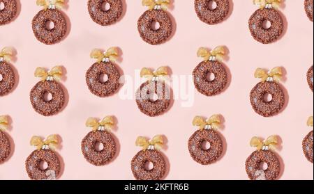 Schokoladen-Donuts-Muster mit goldenen Schleifen auf rosa Hintergrund. weihnachten glasierte Dekorationen -Kugeln Draufsicht von oben Stockfoto