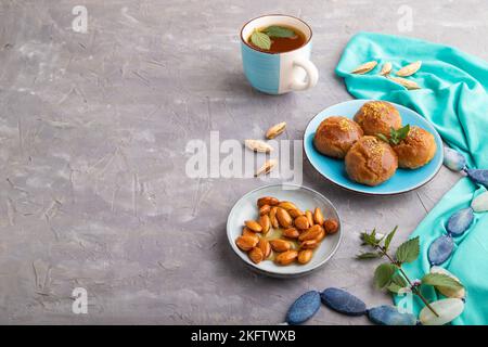 Hausgemachte traditionelle türkische Dessert Sekerpare mit Mandeln und Honig, Tasse grüner Tee auf grauem Beton Hintergrund und blauem Textil. Seitenansicht, Kopie Stockfoto