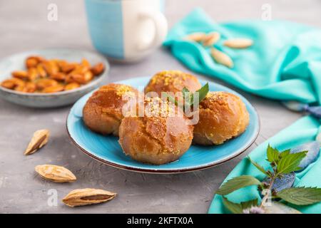 Hausgemachte traditionelle türkische Dessert Sekerpare mit Mandeln und Honig, Tasse grüner Tee auf grauem Beton Hintergrund und blauem Textil. Seitenansicht, selec Stockfoto