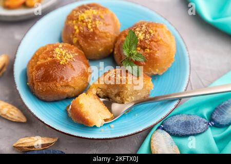 Hausgemachte traditionelle türkische Dessert Sekerpare mit Mandeln und Honig, Tasse grüner Tee auf grauem Beton Hintergrund und blauem Textil. Seitenansicht, selec Stockfoto