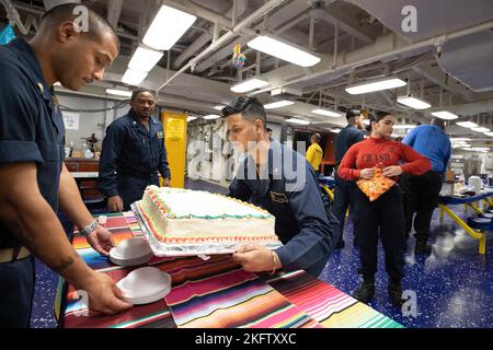 221008-N-IL330-1017 SÜDCHINESISCHES MEER (OKT 8, 2022) – Chief Aviation Maintenance Administrationman Fausto Ferran aus New York, links, und Yeoman 3. Class LAKSHYA Dhiman aus Houston zeigen während des Hispanic Heritage Month einen Kuchen auf den Messdecks an Bord des amphibischen Angriffsträgers USS Tripoli (LHA 7) am 8. Oktober 2022. Tripolis ist im Einsatzgebiet der US-Flotte von 7. tätig, um die Interoperabilität mit Verbündeten und Partnern zu verbessern und als einsatzbereite Einsatztruppe für den Frieden und die Stabilität in der Region Indo-Pazifik zu dienen. Stockfoto