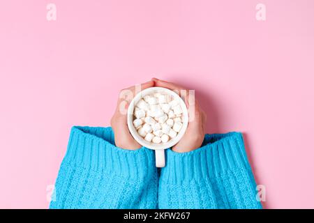 Draufsicht auf Mädchen Hände in blau gemütlich übergroßen Pullover hält große Tasse Kakao oder heiße Schokolade isoliert auf rosa Hintergrund Stockfoto