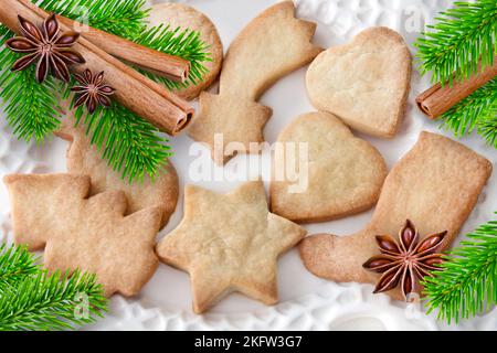 Weihnachtsplätzchen mit Zimt, Tannenzweigen und Anise auf weißem Teller Stockfoto