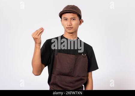 Ein hübscher, asiatischer Barista mit brauner Schürze und schwarzem T-Shirt auf weißem Hintergrund. Barista macht italienische Geste mit Hand und Fingern. Stockfoto