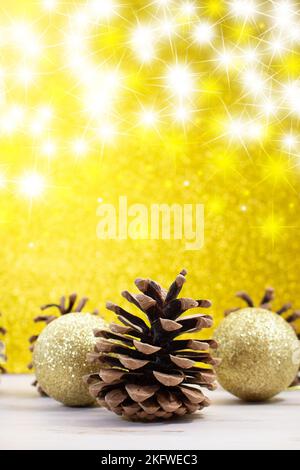 Tannenzapfen mit glänzenden Kugeln auf dem Rücken gelb glänzender Hintergrund mit Sternen. Weihnachten, Neujahr. Vertikal. Speicherplatz kopieren Stockfoto