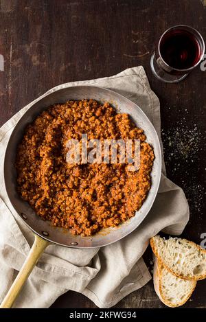 ragù alla Bolognese: Sauce aus frischen Tomaten, Hackbraten, Zwiebeln, Knoblauch und Karotten, serviert auf einer Pfanne auf einem Holztisch. Draufsicht. Stockfoto