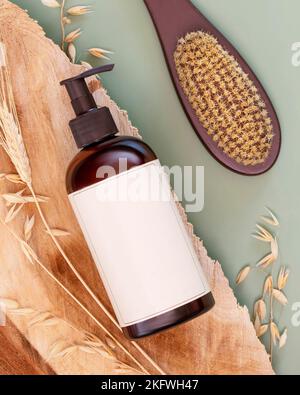 Natürliches Beauty-Produkt. Spenderflasche mit Beauty-Produkt und Duschbürste auf einem Holzpodium auf grünem Hintergrund mit Roggen- und Weizenohren. Moc Stockfoto