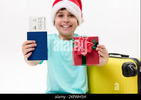 Konzentrieren Sie sich auf eine Bordkarte und ein Weihnachtsgeschenk in den Händen eines charmanten Jungen mit Weihnachtsmütze. Reisen Sie an Weihnachten Winterferien Stockfoto