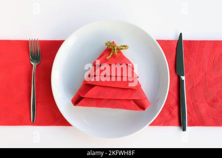 Rote Serviette gefaltet in Kiefernform in Teller mit Besteck-Set.Weihnachten oder Neujahr-Konzept Stockfoto