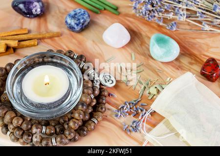 Pflegeleichte, heilende Komposition mit Rosenkranz, Duftstäbchen, Chakra-Steinen, Sandelholz-Stäbchen und Kerze auf einem rosafarbenen Marmorpodium. Konzept von relaxi Stockfoto