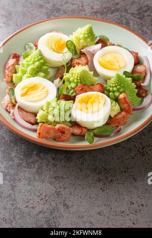 Köstliches Frühstück mit Romanesco-Kohl, gekochten Eiern, gebratenem Speck und Mikrogemüse aus der Nähe auf einem Teller auf dem Tisch. Vertikal Stockfoto