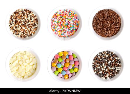 Zucker und Schokolade bestreuen in weißen Schalen. Schokoladenkugeln, Nonpareils, rutenförmiger Zucker und Schoko-Streuseln, weiße Schokoherzen und Knabberartikel. Stockfoto