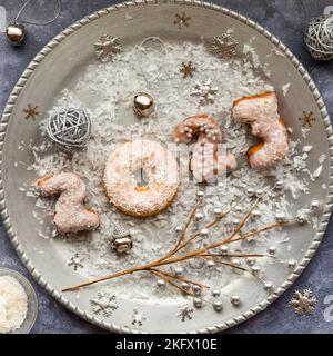 Eine silberne Platte mit Neujahrs-Donuts für 2023, unter festlichen Dekorationen. Stockfoto