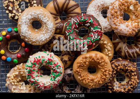 Ein Haufen köstlicher hausgemachter Donuts mit verschiedenen Lasuren und Belägen. Stockfoto