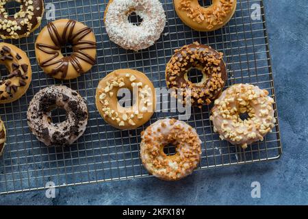 Mehrere frisch zubereitete leckere Donuts mit verschiedenen Belägen, auf einem Kühlregal. Stockfoto