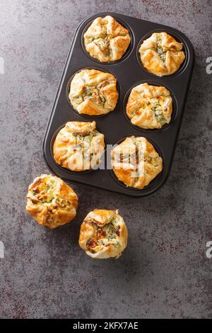 Hausgemachter Spinat-Muffin-Puff mit Feta und Zwiebel in der Maffin-Backform auf dem Tisch. Vertikale Draufsicht von oben Stockfoto