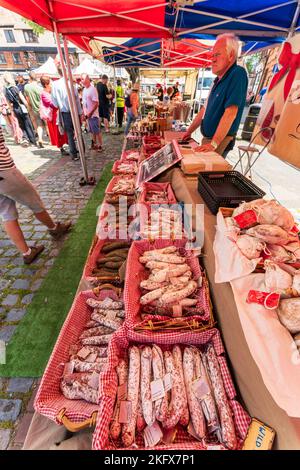 Verschiedene Arten von Französisch getrockneten Fleisch tassisson sec Würstchen, Salami, in Körben zum Verkauf auf dem Freiluftmarkt Stand. Im Hintergrund Menschen und andere Stände Stockfoto