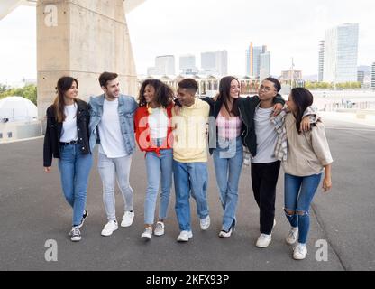 Eine Gruppe von multiethnischen jungen Freunden, die durch die Stadt gehen und lachen und sich gegenseitig halten. Freundschaft und Diversität Konzept Stockfoto
