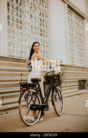 Hübsche junge Frau mit weißem bichon Frisehund im Korb mit Elektrofahrrad Stockfoto