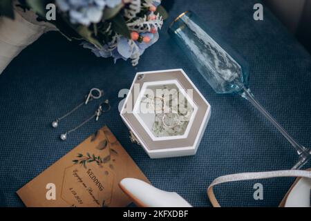 Brautzubehör. Blumen, Parfüm, Ringe in Glasbox, Einladung, Schuhe. Stockfoto