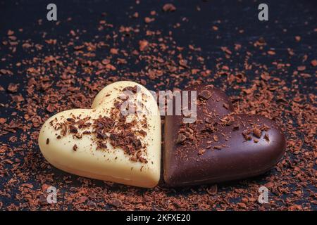 Zwei herzförmige Pralinen aus Milch und weißer Schokolade auf der Schiefertafel, mit geriebener Schokolade überzogen. Desserts zum Valentinstag. Stockfoto