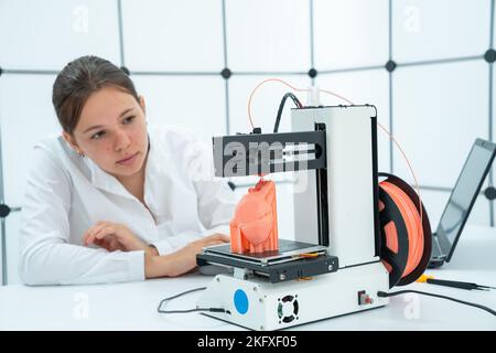 3D Drucken eines Modells eines menschlichen Herzens auf einem Drucker von 3D beobachtet eine junge Studentin den Druckprozess von 3D Stockfoto