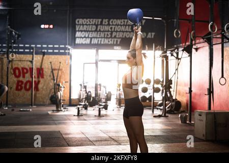 kaukasisches Mädchen in Sportkleidung, das körperliche Übungen mit einem großen schweren Ball auf dem Kopf macht Stockfoto