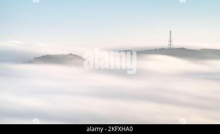 Der Funkmast auf Norwood Edge und ein nahegelegener Hügel sind während einer Herbsttemperaturinversion in North Yorkshire über einem rollenden Nebelmeer sichtbar. Stockfoto