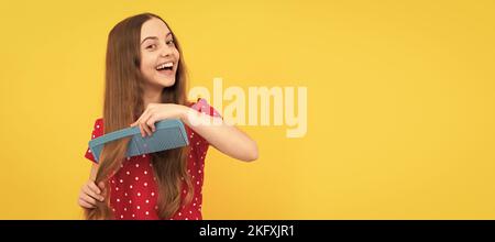 Happy Kid Kämmen lange Haare. Friseur. Mädchen hat wellige Frisur halten Haarbürste. Teen Schönheit Frisur. Kid girl Haarpflege, horizontales Poster. Banner Stockfoto