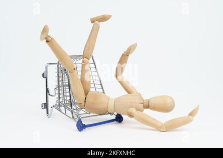 Geschäftskonzept. Der Holzmann fiel vom Einkaufswagen auf den Boden. Isoliert auf weißem Hintergrund. Stockfoto