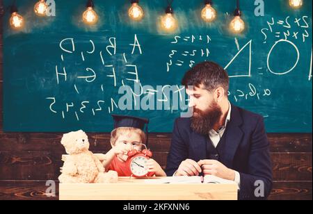 Der junge männliche Lehrer führt seinen Schüler zum Lernen, während er im Klassenzimmer mit Kritzeleien auf dem Schwein sitzt Stockfoto