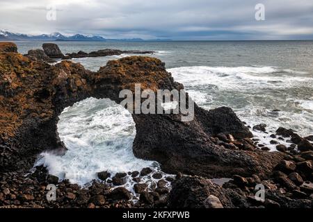 Wellen stürzen durch Gattlekur oder den Hellnar Arch, einen natürlichen Steinbogen, der zwischen Arnarstapi und Hellnar auf der isländischen Halbinsel Snæfellsnes gefunden wurde. Au Stockfoto