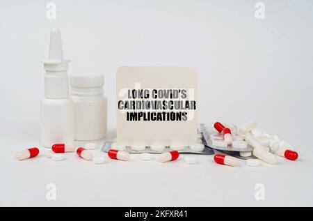 Medizinisches Konzept. Auf einer weißen Oberfläche, Blasen, Tabletten, Spray und ein Schild mit der Aufschrift - lange COVID kardiovaskuläre Implikationen Stockfoto