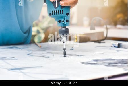 Der Mechaniker verwendet einen elektrischen Schraubendreher oder einen elektrischen Bohrer, um die Mutter an der Metallplatte zu befestigen Stockfoto