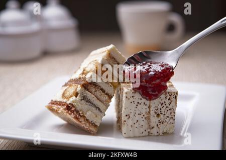 Ein Nahaufnahme-Studiofoto des Löffelens von Erdbeergelee auf Tiramisu-Kuchen auf einem weißen Teller. Stockfoto