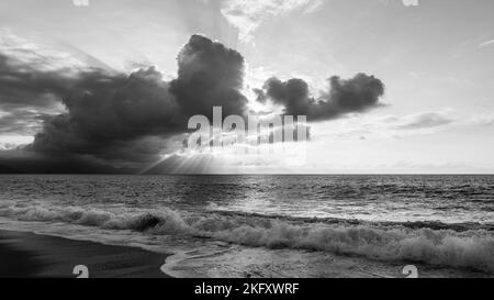 Ein Sonnenuntergang Am Meer Mit Sonnenstrahlen, Die Hinter Den Wolken Schwarz Und Weiß Ausstrahlen Stockfoto