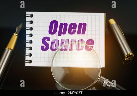 Wirtschaft und Handel. Auf der schwarzen Oberfläche befindet sich ein Stift, eine Lupe und ein Notizbuch mit der Aufschrift - Open Source Stockfoto