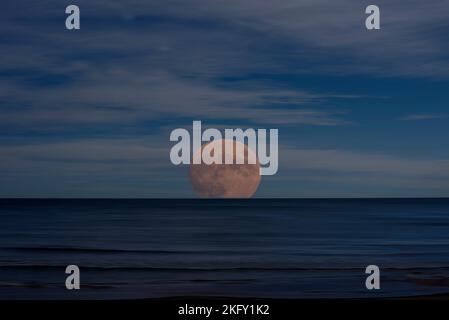 Foto des über dem Meer aufgehenden Mondes. Illustration. Ruhiges Wasser mit beweglicher Wirkung, dunkle, sich bewegende Wolken, Foto als Zeichnung Stockfoto