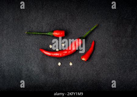 Rote, scharfe Chilischoten und halb gebrochene Chilischoten auf schwarzem Hintergrund Stockfoto