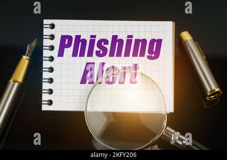 Wirtschaft und Handel. Auf der schwarzen Oberfläche befindet sich ein Stift, eine Lupe und ein Notizbuch mit der Aufschrift - Phishing Alert Stockfoto