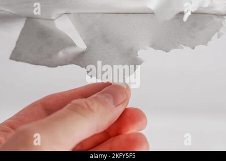 Entfernen einer Schicht alter weißer Farbe von Hand aus der Decke aus nächster Nähe. Abblätterndes Weißes Stockfoto
