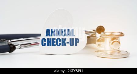 Medizinisches Konzept. Auf der weißen Oberfläche befindet sich ein Stethoskop, daneben befindet sich eine herzförmige Platte mit der Aufschrift - JAHRESKONTROLLE Stockfoto