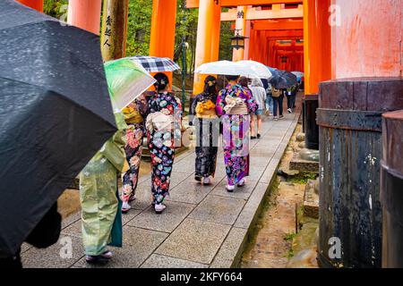 Menschen, die traditionellen Kimono tragen, passieren rote Tore bei Fushimi Inari Taisha in Kyoto, Japan Stockfoto