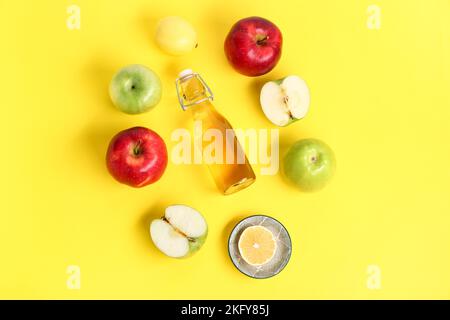 Zusammensetzung mit einer Flasche Apfelessig und Früchten auf gelbem Hintergrund Stockfoto