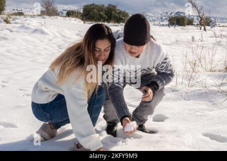 Mutter und Sohn spielen mit Schneebällen auf schneebedecktem Feld Stockfoto